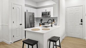 A modern kitchen with white cabinetry, stainless steel appliances, and a central island with stools. - CozySuites at Chandler (Chandler)