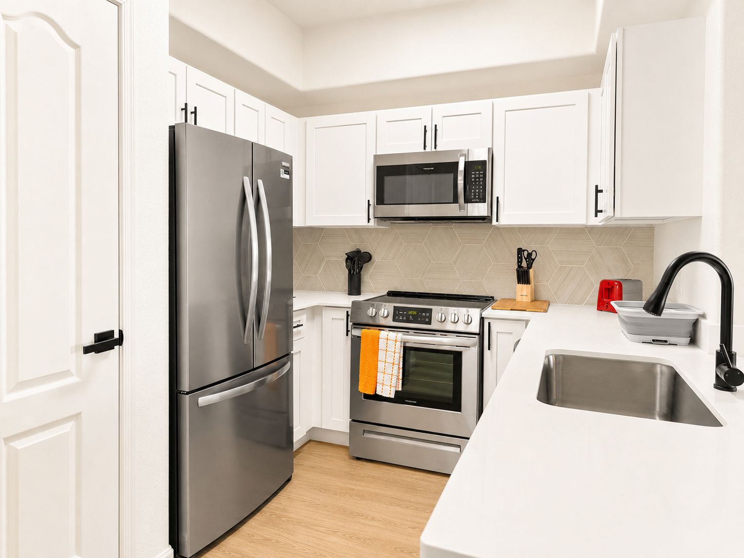 Una cocina moderna con armarios blancos, electrodomésticos de acero inoxidable y piso de madera.