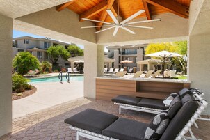 Uma área de estar coberta ao ar livre, com espreguiçadeiras e uma piscina ao fundo.