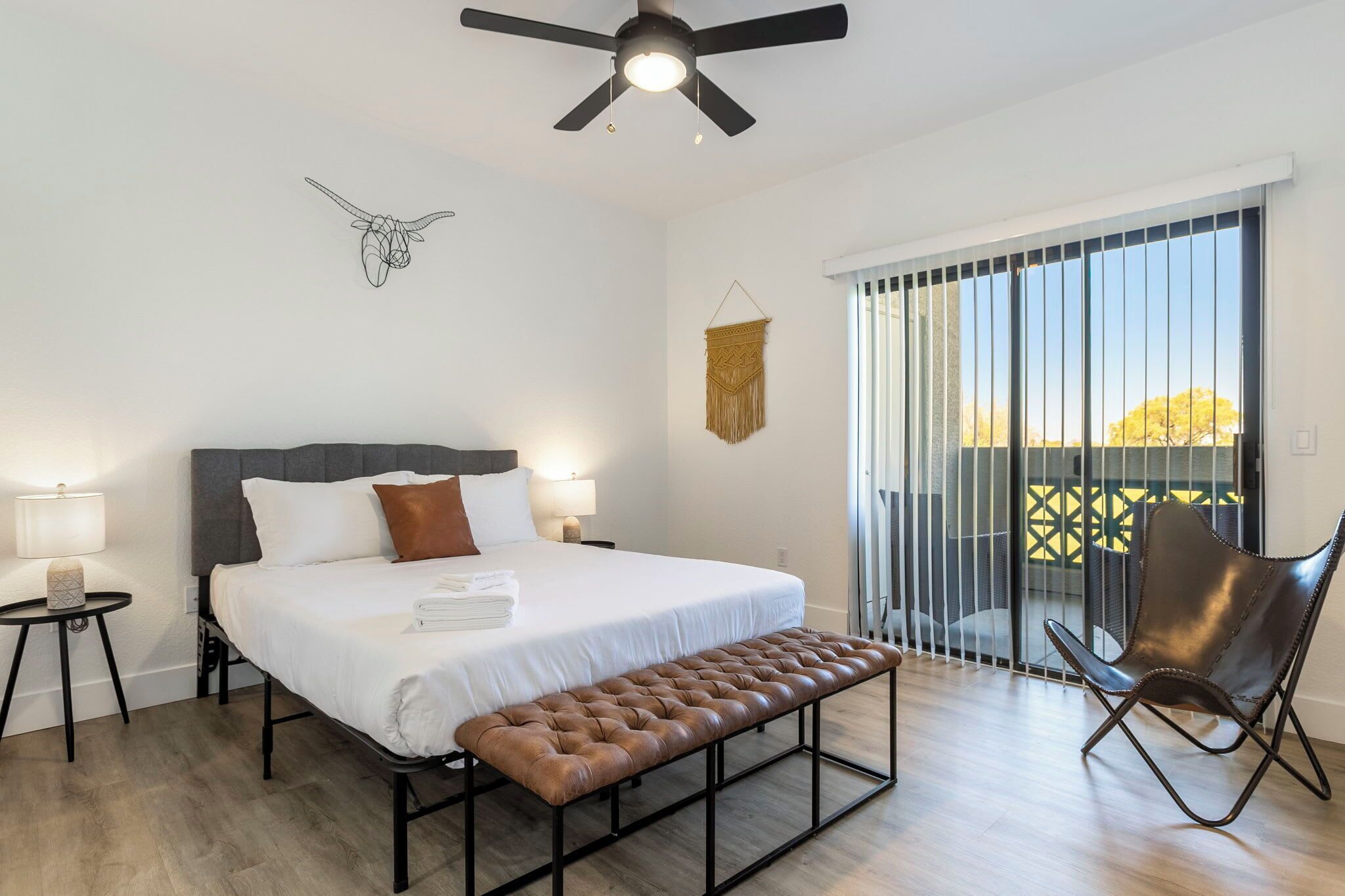 A modern bedroom with a bed, bench, chair, and a ceiling fan.