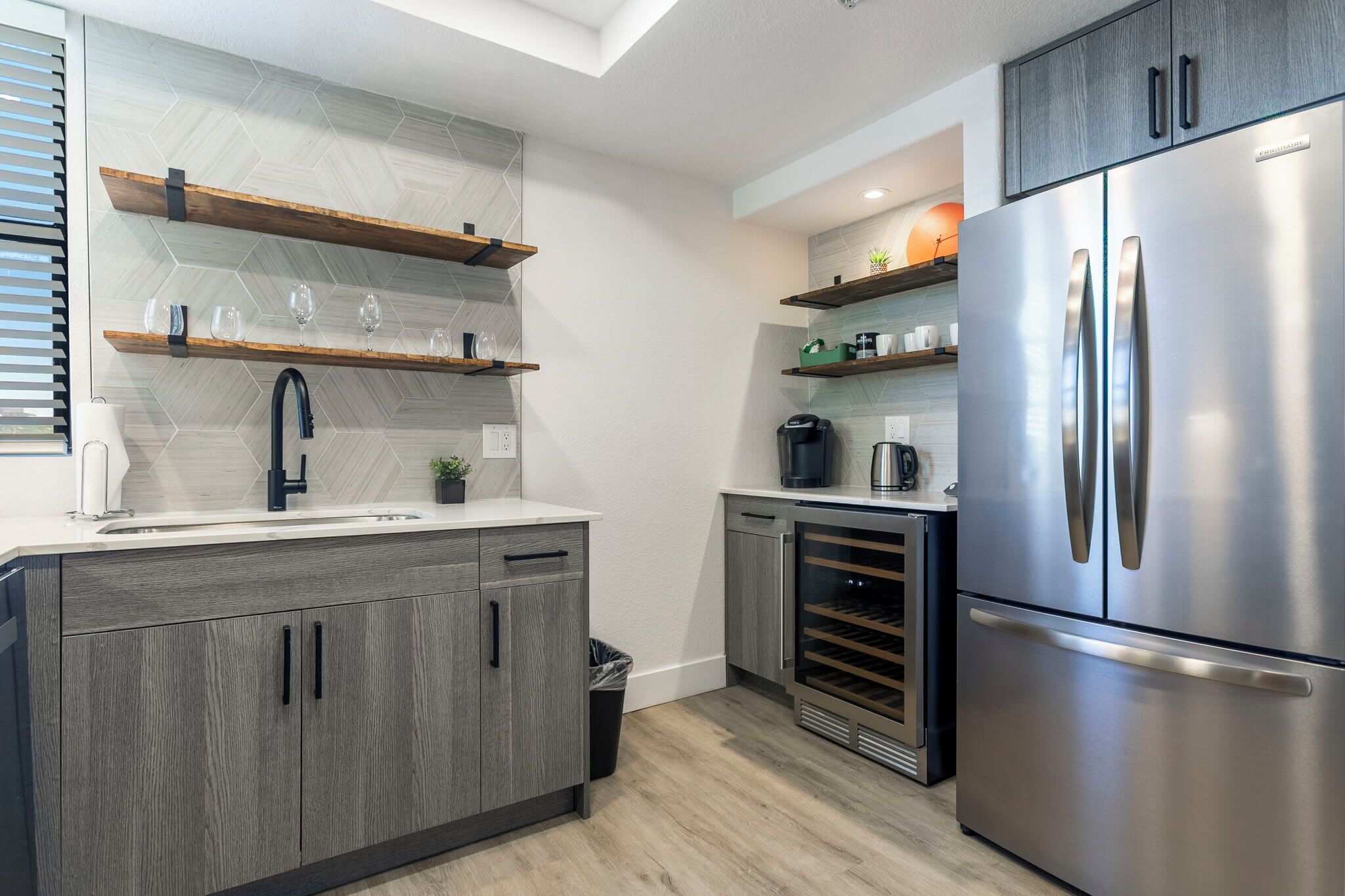 Una cucina moderna con forno a incasso, frigorifero in acciaio inox, mensole in legno e un rubinetto nero.