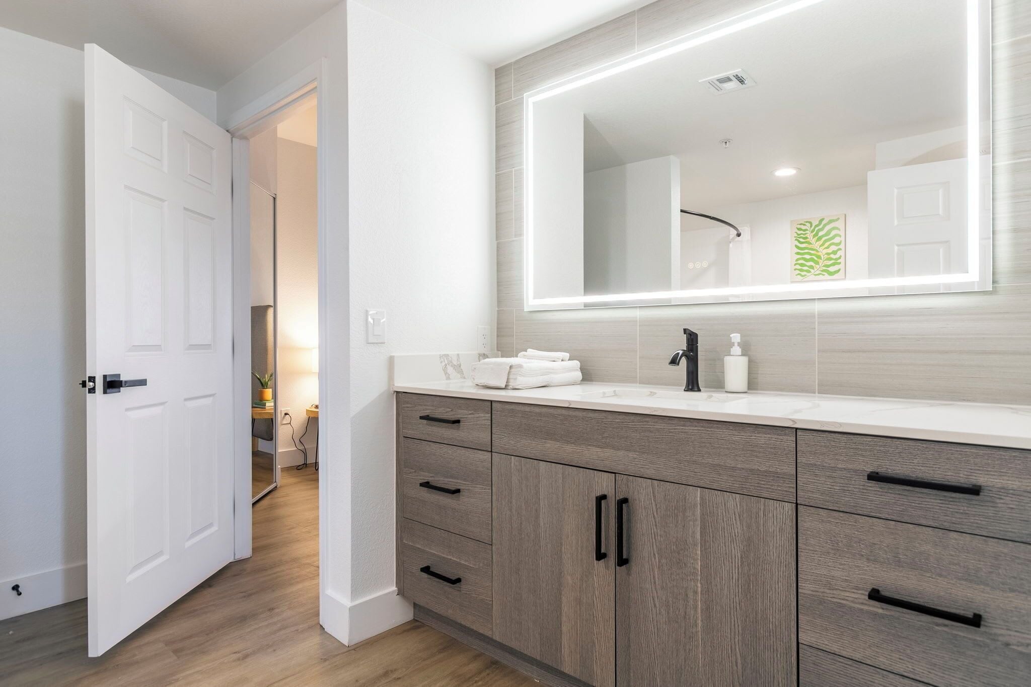 A modern bathroom with a large mirror, white countertop, and wooden cabinets.
