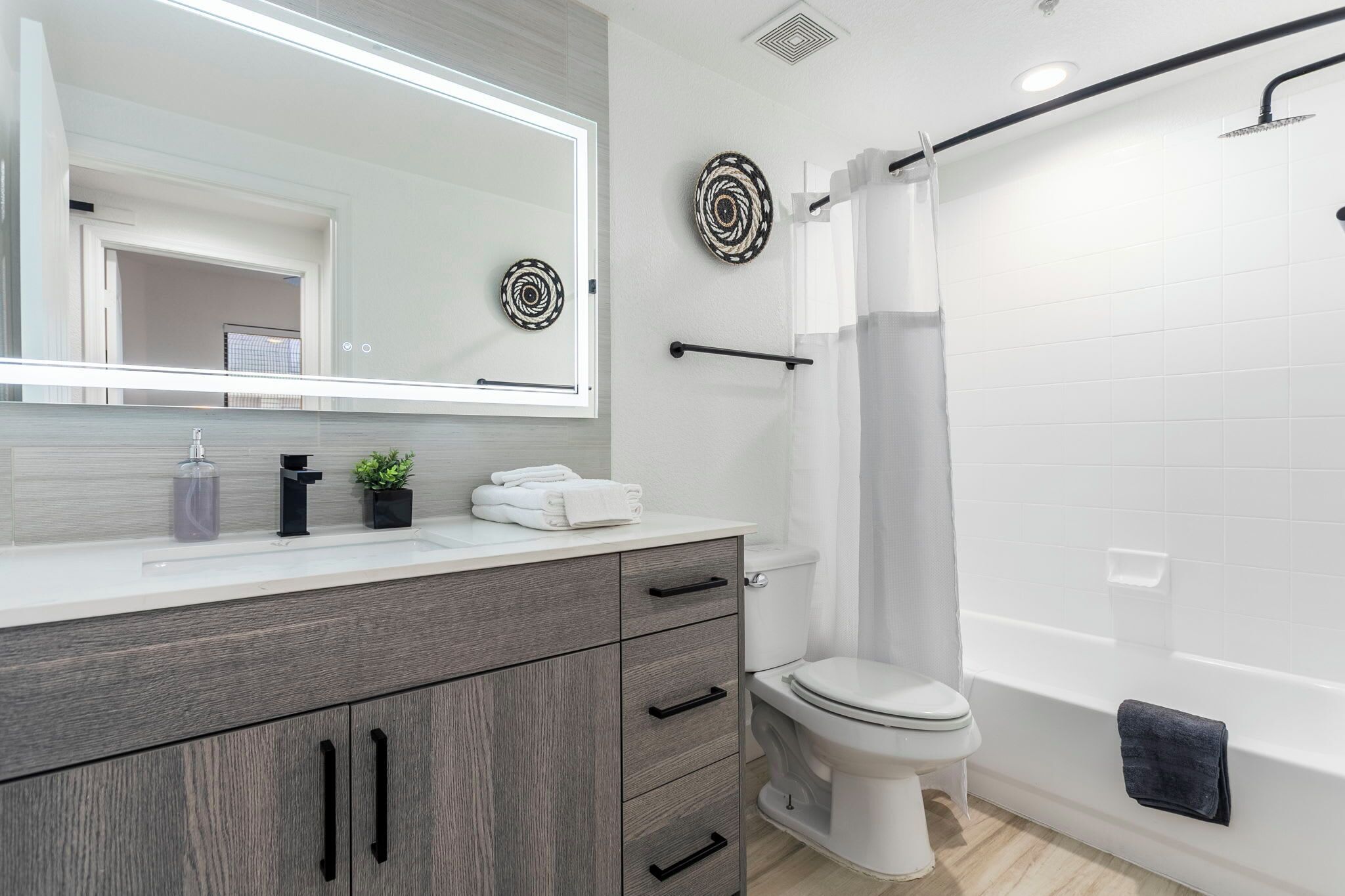 A modern bathroom with a large mirror, a toilet, a bathtub, and a shower curtain.