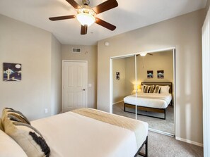 A bedroom with a bed, a ceiling fan, a door, and a mirror. - CozySuites at Kierland Commons (Scottsdale)