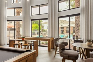A poolside bar with wooden furniture and large windows overlooking a pool area. - CozySuites at Glendale (Glendale)