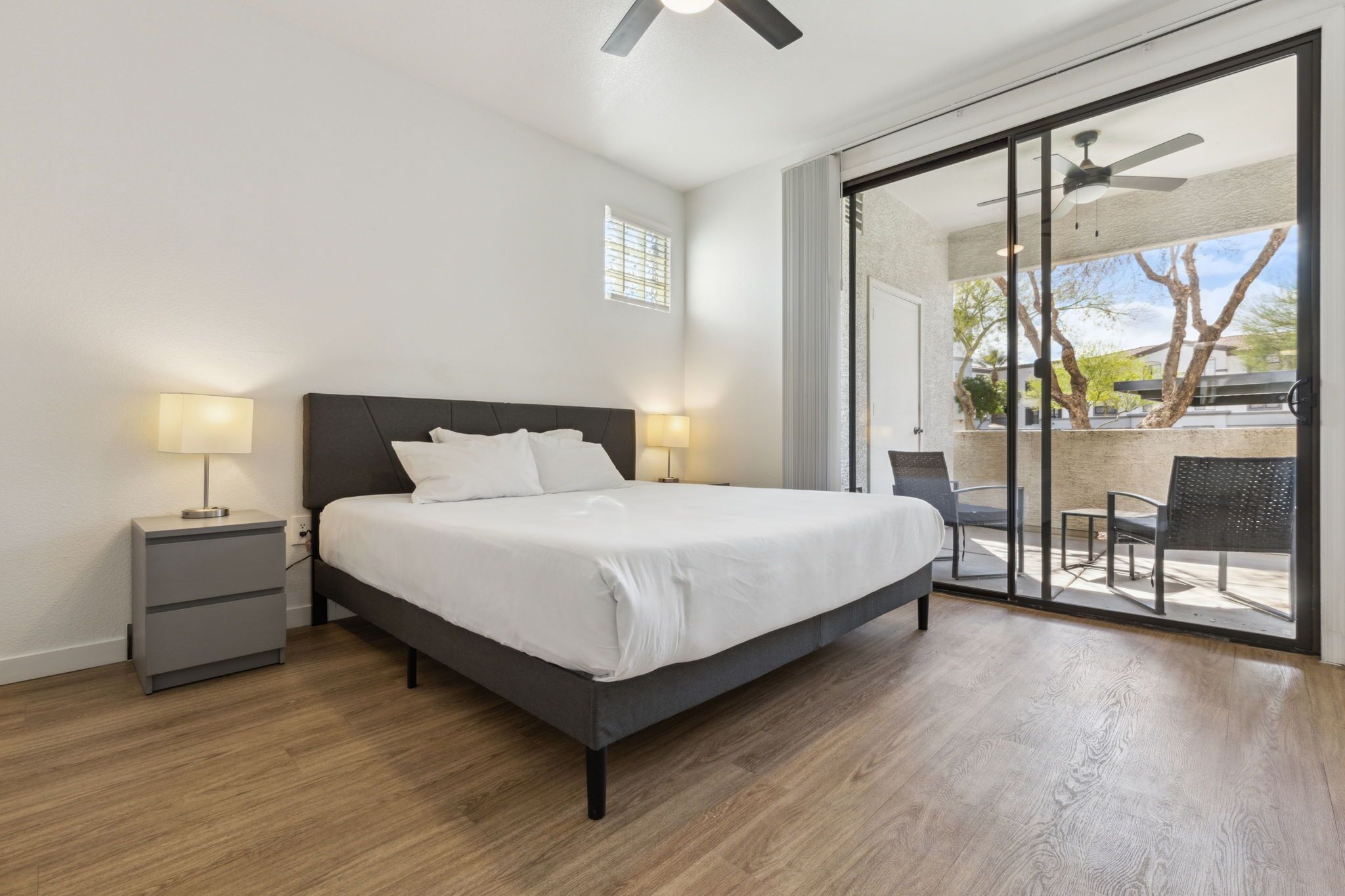 Une chambre à coucher comprenant un lit, des tables de chevet, un ventilateur de plafond et une porte-fenêtre coulissante donnant sur un espace extérieur.