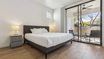 Une chambre à coucher comprenant un lit, des tables de chevet, un ventilateur de plafond et une porte-fenêtre coulissante donnant sur un espace extérieur.