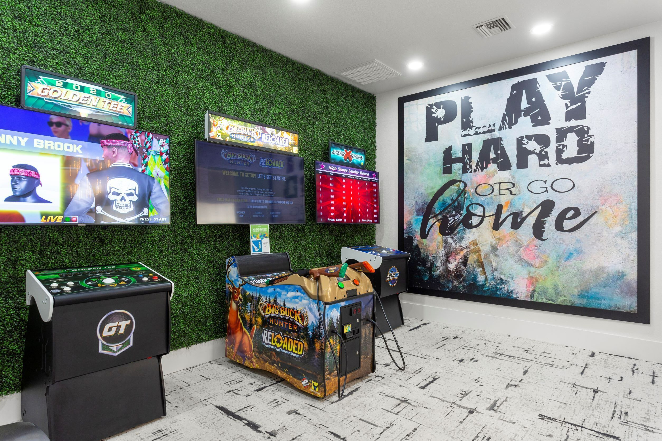 A gaming area with multiple arcade machines, a large motivational poster, and a green wall with a textured pattern.
