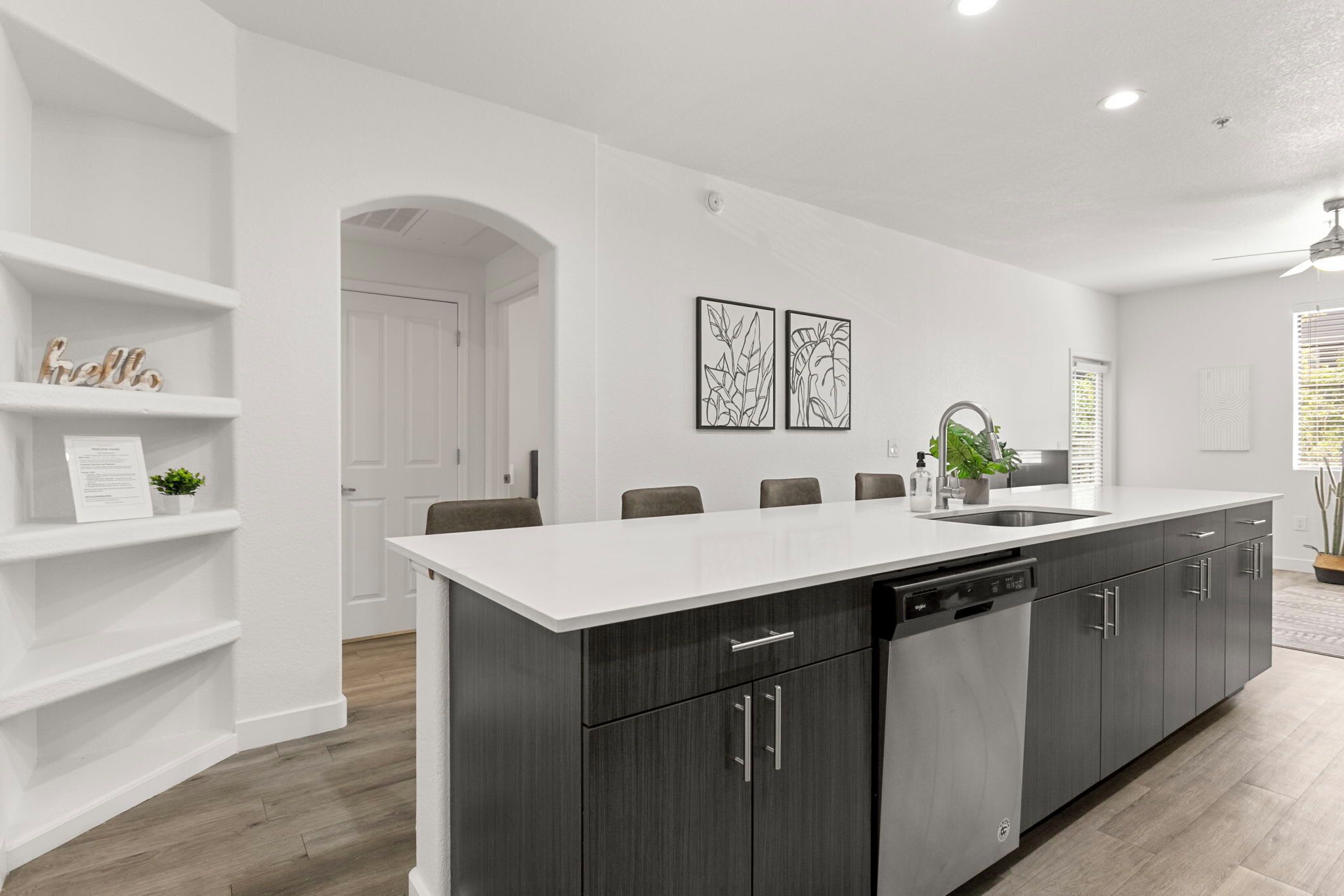 Una cocina moderna con una isla central, muebles oscuros y encimeras blancas.