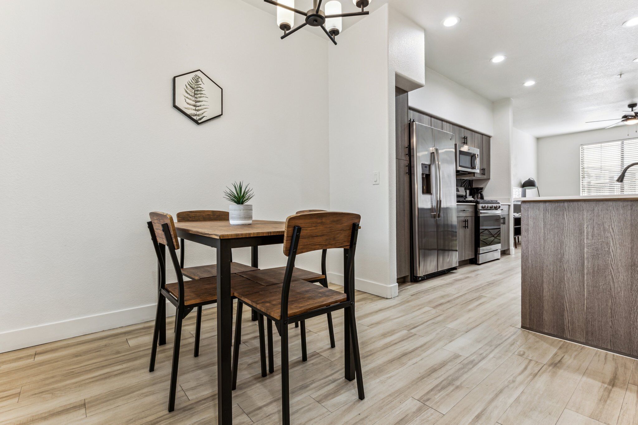 A modern kitchen with a dining area, featuring a wooden table and chairs, a refrigerator, and a microwave.