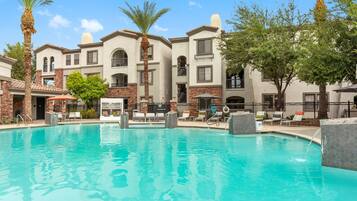 A swimming pool with lounge chairs and palm trees, surrounded by multi-story buildings with balconies.