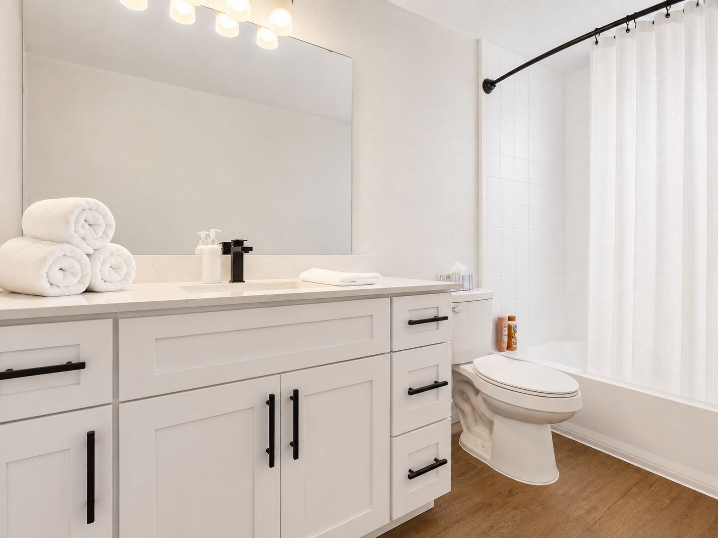 A modern bathroom with a white vanity, a large mirror, a toilet, and a shower curtain.