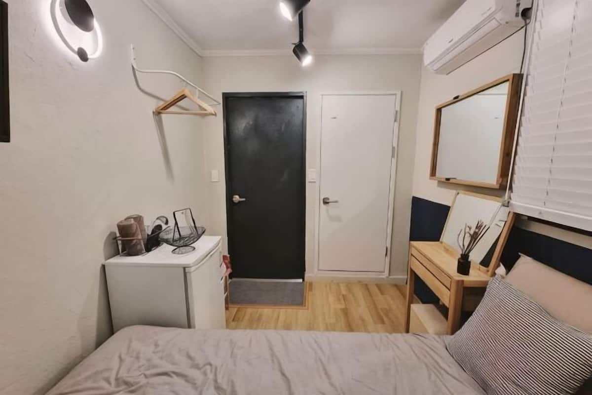 Un dormitorio con una cama, un escritorio, una silla, una mesita, un espejo y una puerta.