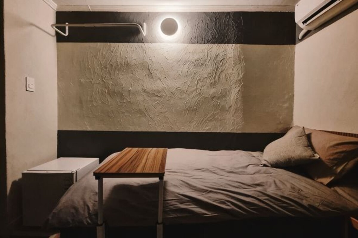 A bedroom with a bed, bedside table, and a wall-mounted light fixture.