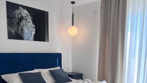 A modern bedroom with a blue headboard, a large bed with white bedding, a single nightstand, a wall-mounted light fixture, and a framed picture of a lion.