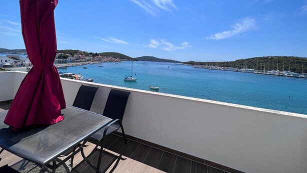 A balcony with a view of a calm sea, boats, and a hilly landscape.