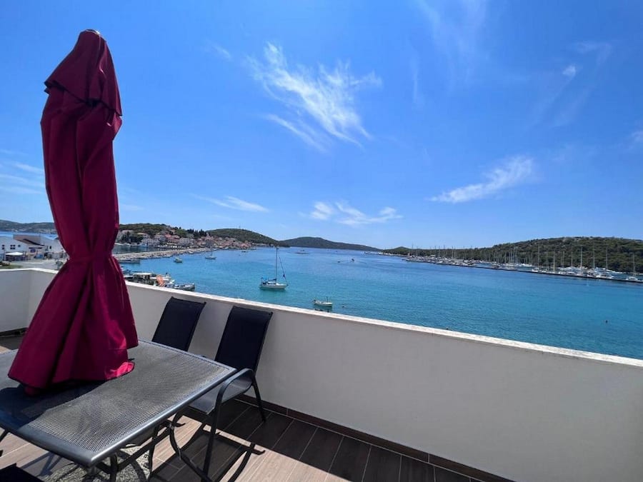 A balcony with a view of a calm sea, boats, and a hilly landscape.