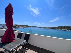A balcony with a view of a calm sea, boats, and a hilly landscape.
