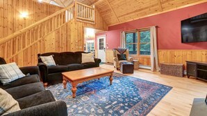 Een houten interieur met een trap, een zwarte bank, een houten salontafel en een groot raam.