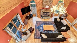 Een gezellig interieur met een stenen open haard, houten wanden, een zwarte bank, een houten salontafel en een televisie.