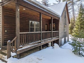 Una cabaña de madera con porche, ventanas amplias y suelo cubierto de nieve.