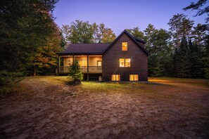 A two-story log cabin with a balcony, surrounded by a forest. - Maine Lodge with Fireplace and Pool Table (Bethel)
