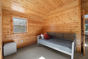 A small, cozy room with wooden walls, a single window, a bench with cushions, and a carpeted floor. - Maine Lodge with Fireplace and Pool Table (Bethel)