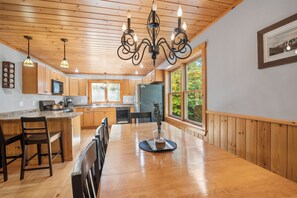 A spacious kitchen with wooden cabinets, a central island, and a dining area with a large table. - Maine Lodge with Fireplace and Pool Table (Bethel)