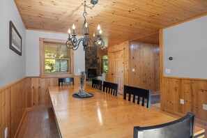 A wooden-paneled dining room with a large table, chairs, and a chandelier. - Maine Lodge with Fireplace and Pool Table (Bethel)