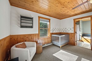 A room with a crib, a sofa, a window, and a wall with tree decals. - Maine Lodge with Fireplace and Pool Table (Bethel)
