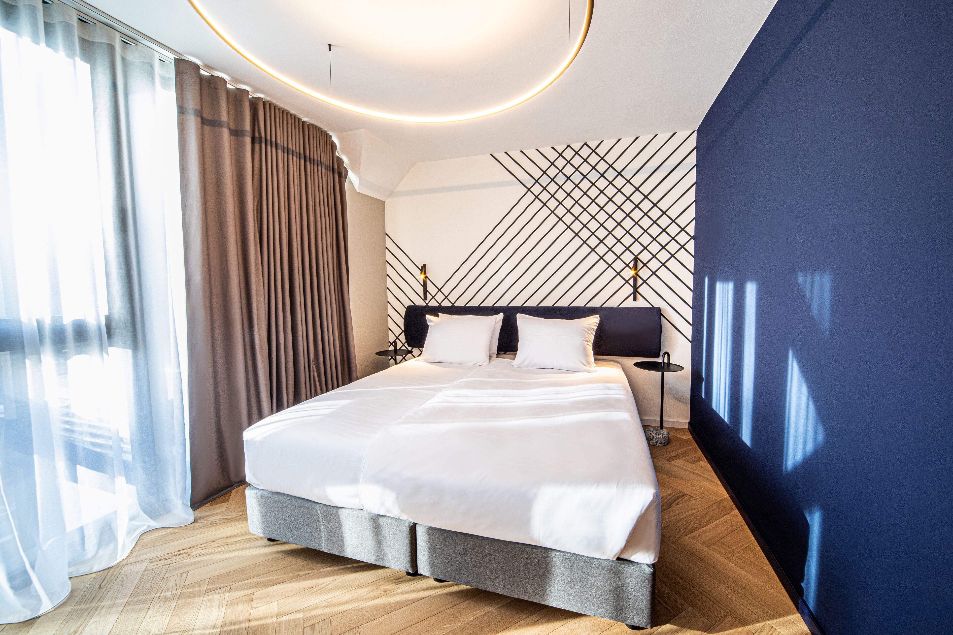 Habitación de hotel moderna con una cama grande, piso de madera, pared azul decorativa y un diseño geométrico en la pared.