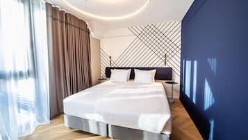 A modern hotel room with a large bed, a wooden floor, a blue accent wall, and a geometric wall design.