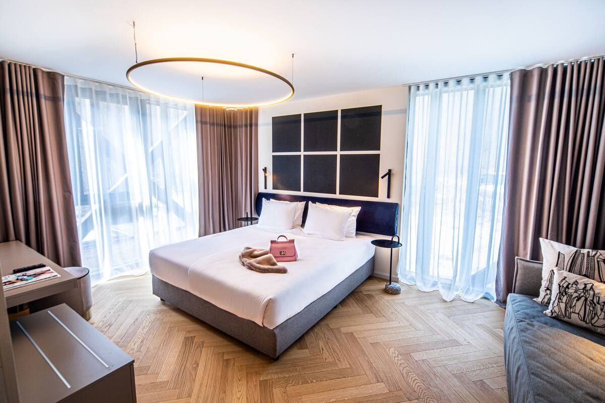 A modern hotel room with a large bed, a desk, and a sofa.
