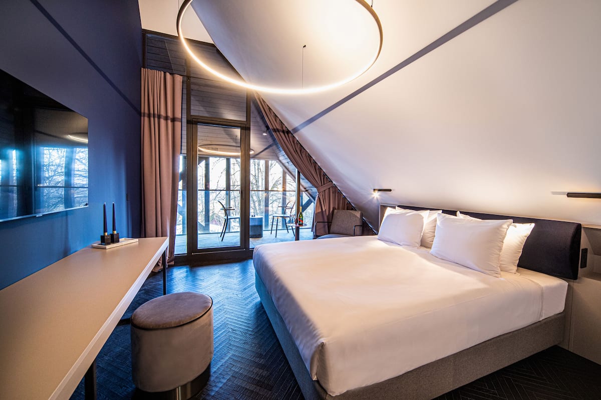A modern hotel room with a large bed, a desk, and a view of the outdoors.