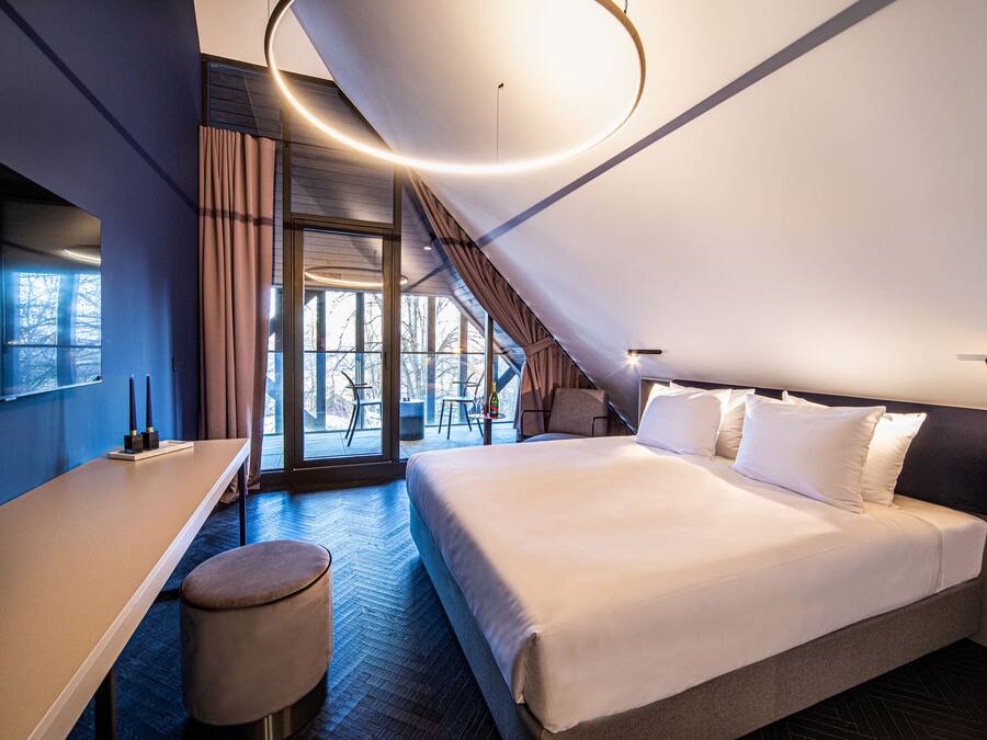 A modern hotel room with a large bed, a desk, and a view of the outdoors.