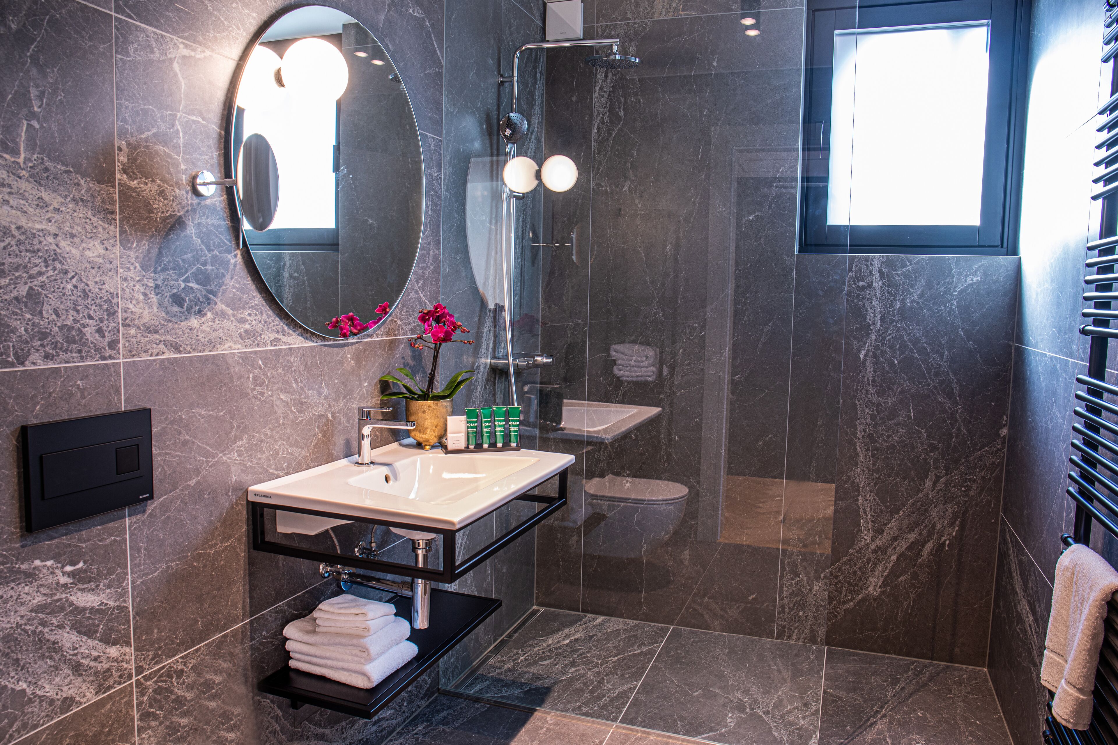Une salle de bain moderne avec un sol en marbre, un miroir rond, un lavabo avec un porte-serviettes et un espace douche.