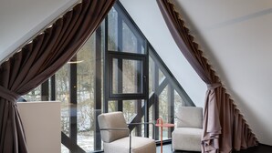 Una habitación moderna con un ventanal grande, un sofá, una silla y una mesita.
