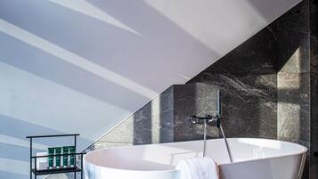 Un bagno moderno con una vasca freestanding, uno scaffale con articoli da toilette e un pavimento in marmo.