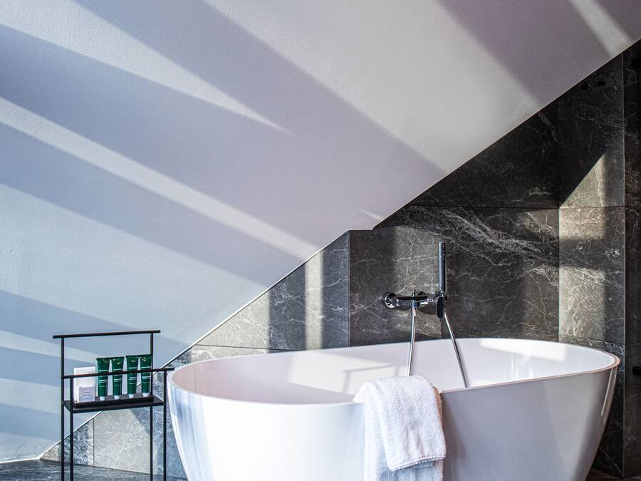 Un bagno moderno con una vasca freestanding, uno scaffale con articoli da toilette e un pavimento in marmo.