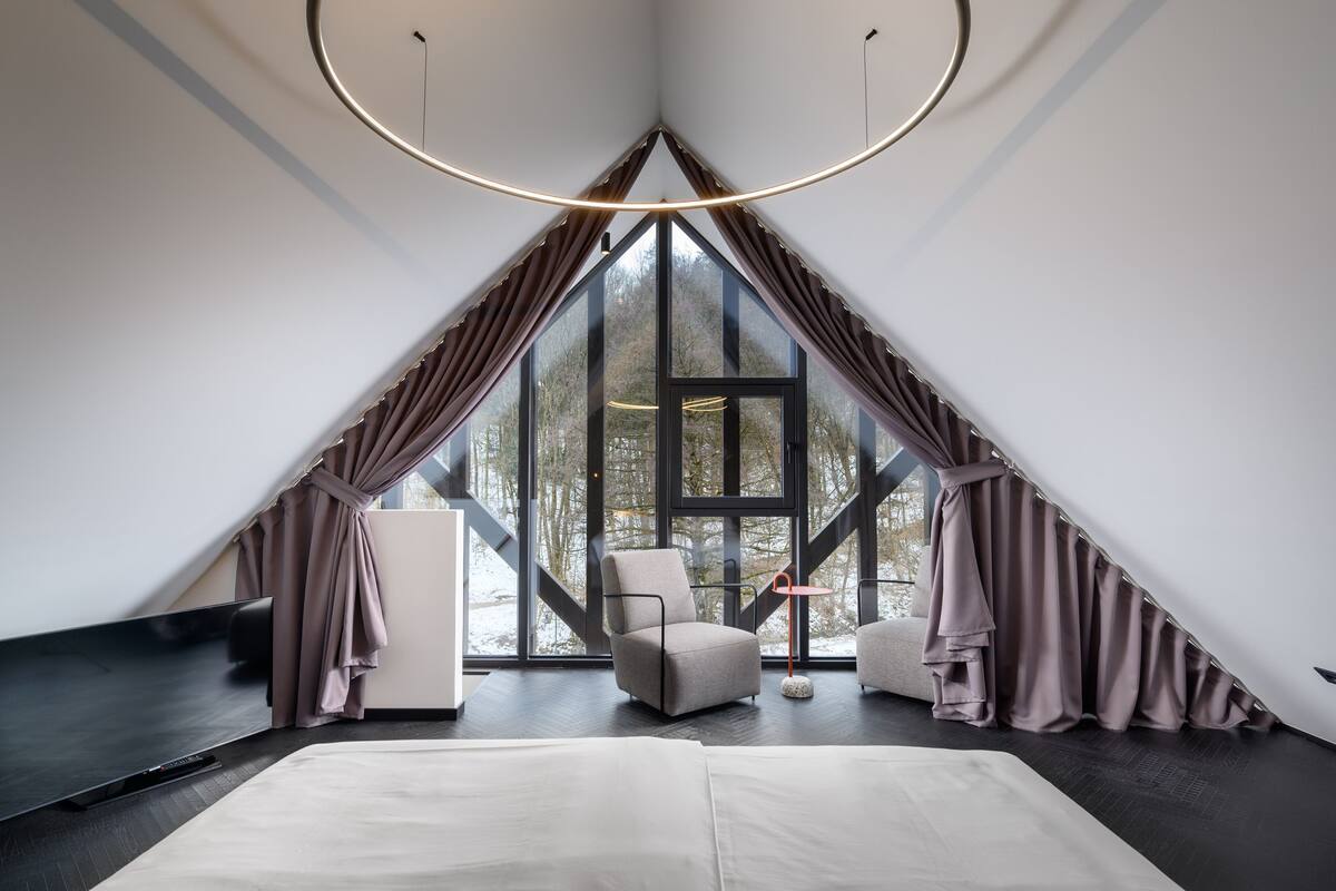 A modern room with a large window, a bed, a chair, and a television.