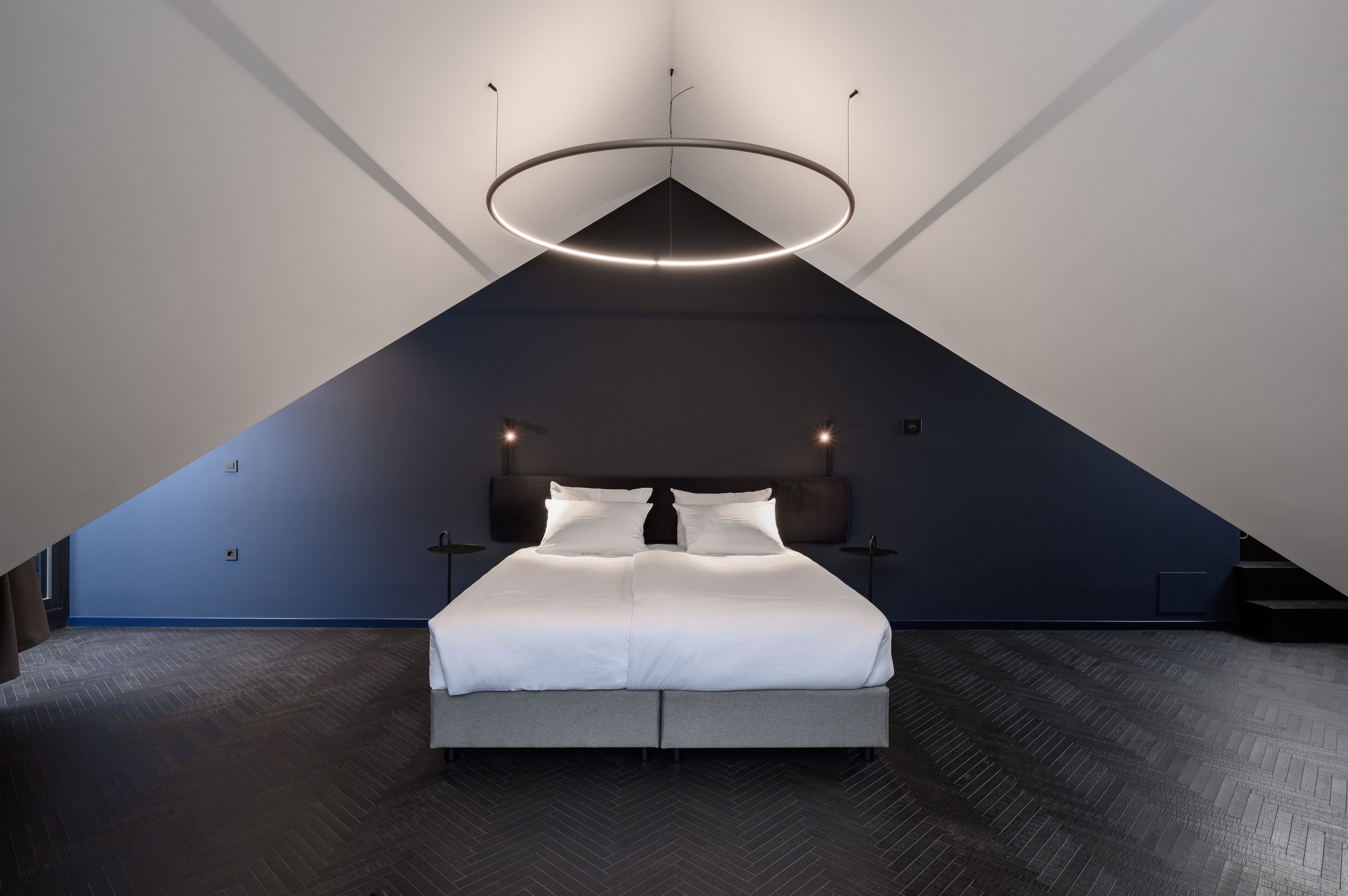 A modern bedroom with a large bed, a circular ceiling light, and a sloped ceiling.