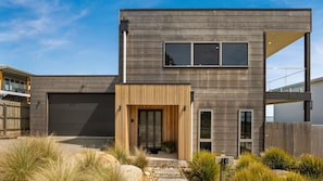 Una casa moderna de dos pisos con garaje, puerta principal de madera y un pequeño jardín con rocas y plantas.