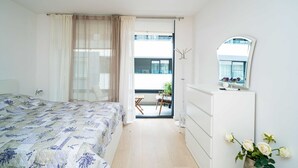 Un dormitorio con cama, cómoda, espejo y vista al balcón.