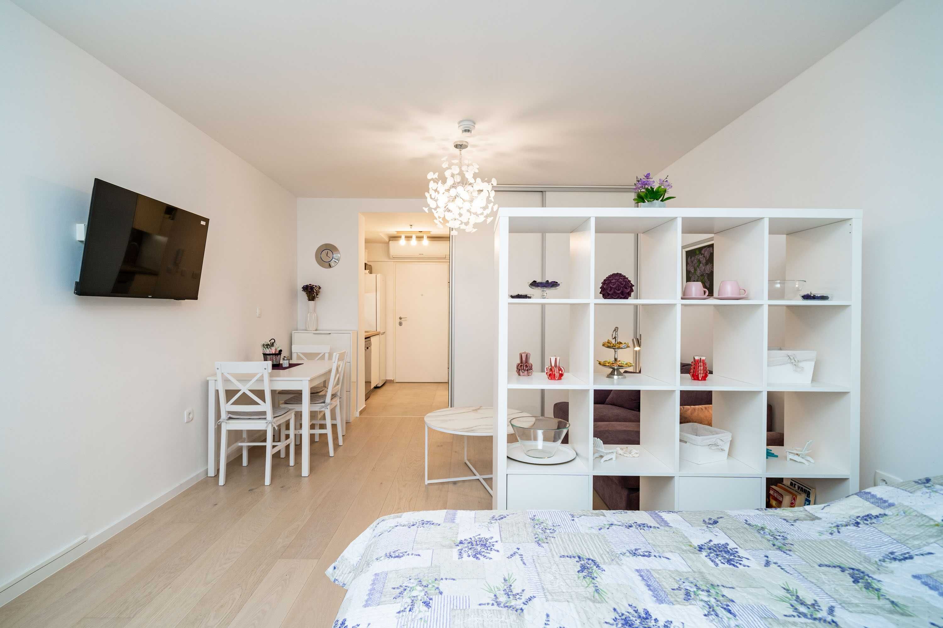 Une chambre à coucher moderne avec un lit, une armoire blanche, un bureau avec des chaises et un lustre.