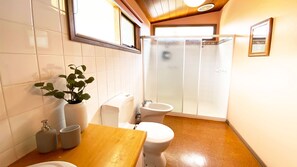 Une salle de bain comprenant des toilettes, un bidet, un lavabo et une douche avec une porte en verre.