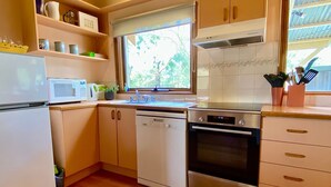 Eine kompakte Küche mit Mikrowelle, Geschirrspüler, Backofen und einem Fenster mit Blick auf Bäume.