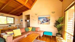 Ein gemütliches Wohnzimmer mit Holzboden, einer Couch mit Kissen, einem Couchtisch und einem Gemälde mit Küstenansicht.