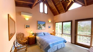Ein Schlafzimmer mit einem Bett, zwei Nachttischen, einem Sessel und einem großen Fenster mit Jalousien.