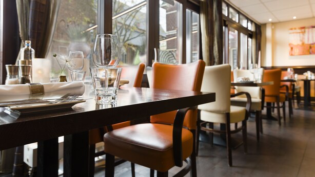 Un comedor con una mesa dispuesta para dos personas, que incluye una botella, vasos y una servilleta doblada.