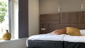 Un dormitorio moderno con una cama grande, una ventana con cortinas, un cabecero de madera y dos lámparas colgantes.